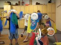 Children wearing paper plate masks and holding scarves.